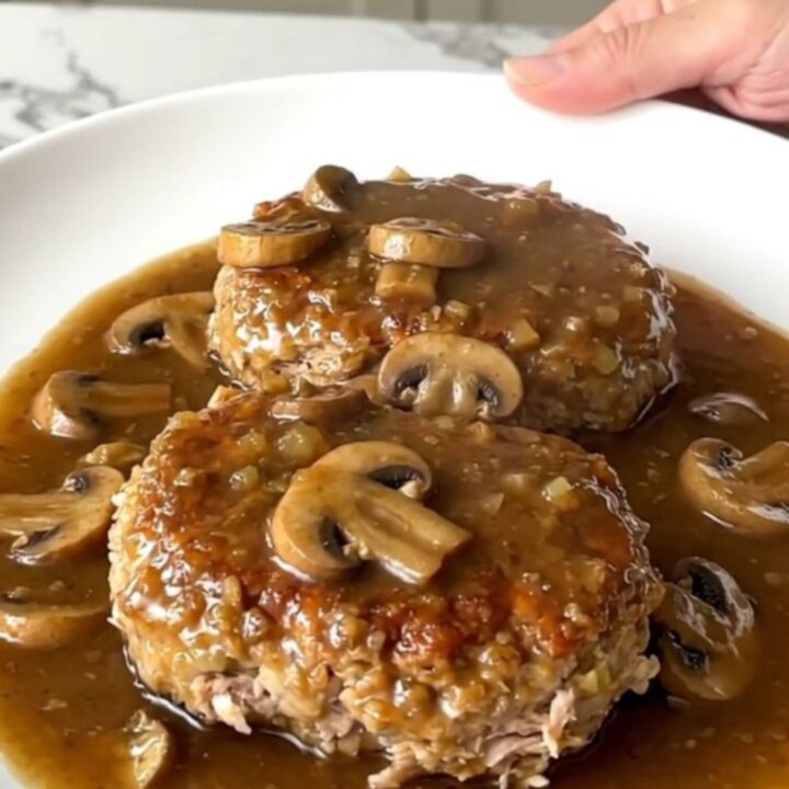A serving spoon lifting a tender turkey Salisbury steak covered in rich mushroom gravy from a slow cooker.