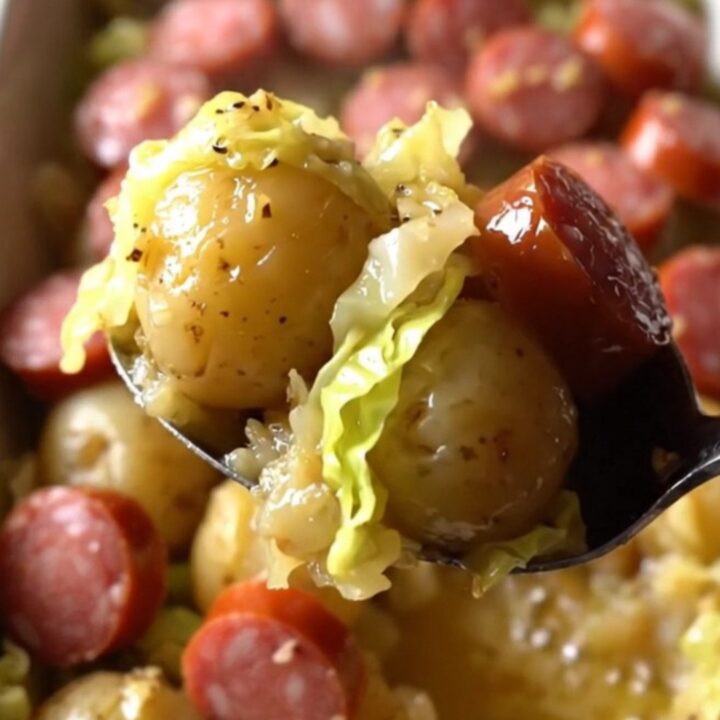 A top-down view of a rectangular baking dish filled with raw cabbage, halved potatoes, and smoked sausage coins.