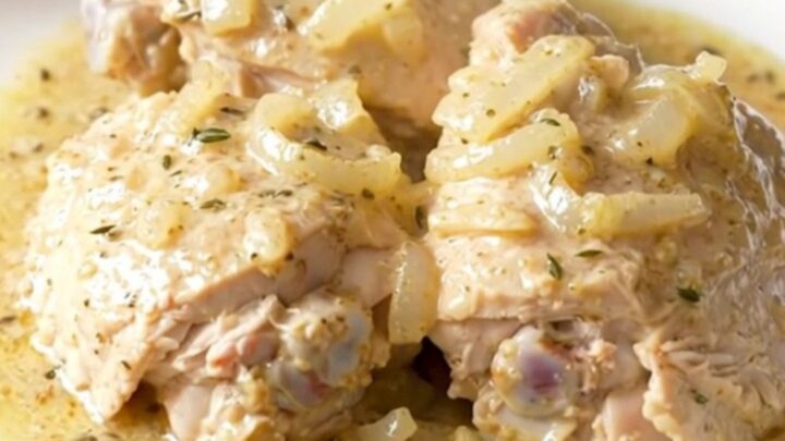 A white plate filled with tender, creamy white wine chicken thighs garnished with fresh herbs.