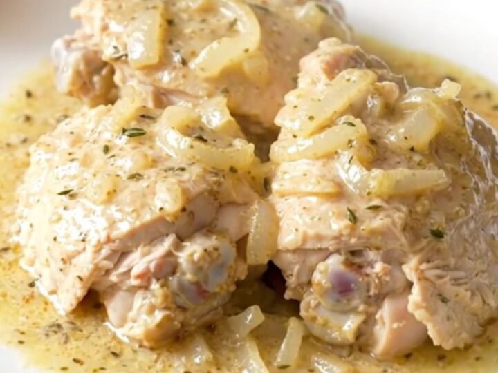 A white plate filled with tender, creamy white wine chicken thighs garnished with fresh herbs.