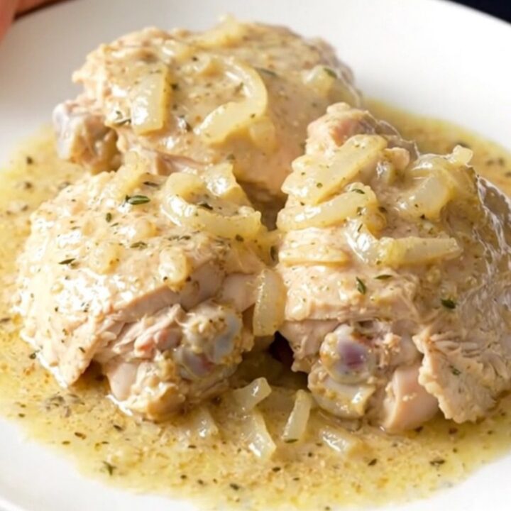 A white plate filled with tender, creamy white wine chicken thighs garnished with fresh herbs.
