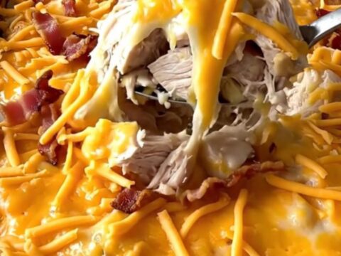 A top-down view of a rectangular baking dish filled with cubed chicken and potatoes topped with cheese and bacon.