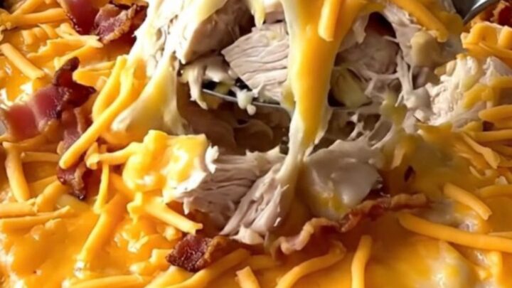 A top-down view of a rectangular baking dish filled with cubed chicken and potatoes topped with cheese and bacon.