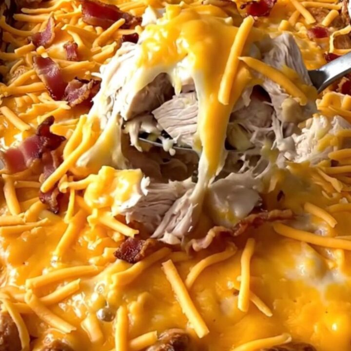 A top-down view of a rectangular baking dish filled with cubed chicken and potatoes topped with cheese and bacon.