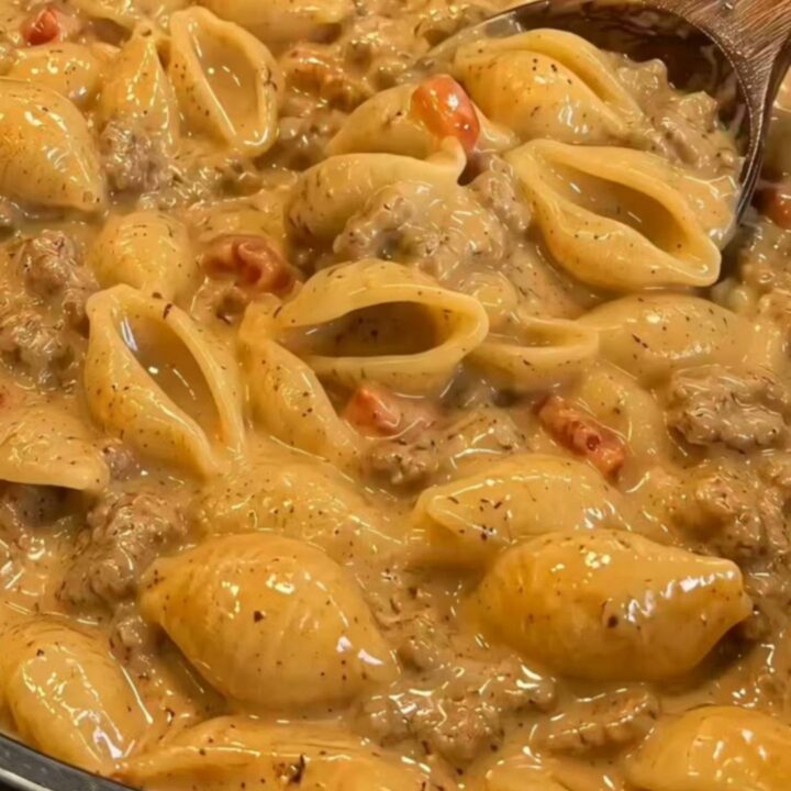 A wooden spoon lifting glossy shell pasta dripping in a rich, seasoned taco-cheese sauce from a skillet.