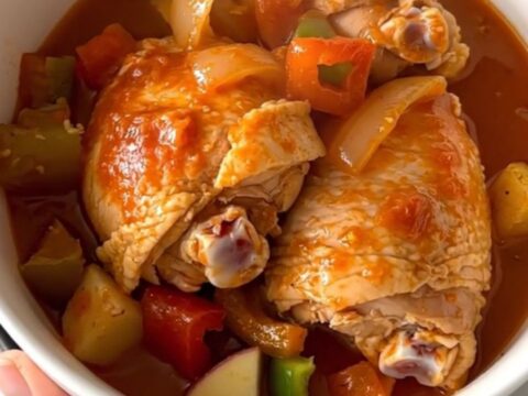 A close-up of slow-cooked pollo guisado served in a white bowl with visible chicken, potatoes, and thick sauce.