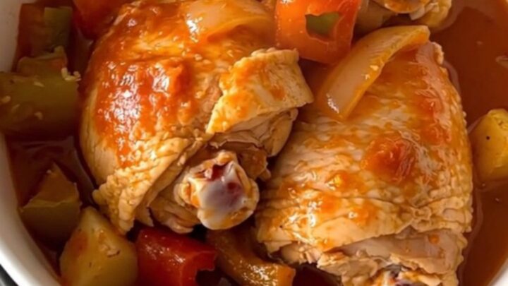 A close-up of slow-cooked pollo guisado served in a white bowl with visible chicken, potatoes, and thick sauce.