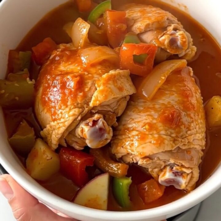 A close-up of slow-cooked pollo guisado served in a white bowl with visible chicken, potatoes, and thick sauce.
