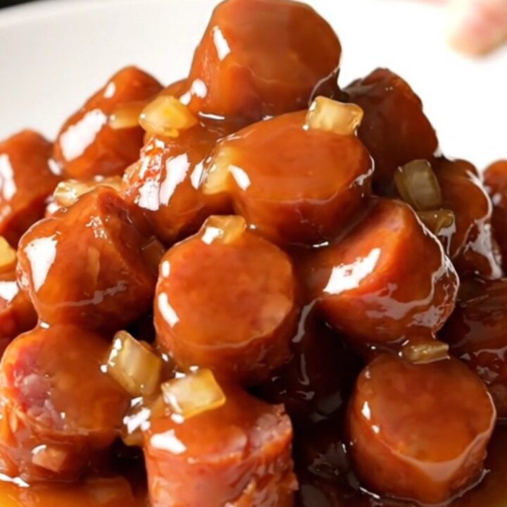 A slow cooker filled with golden-brown kielbasa coins coated in a thick, shiny honey barbecue sauce with bits of onion.