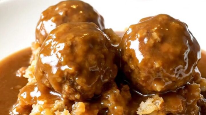 A slow cooker filled with turkey meatballs and stuffing covered in rich brown gravy.