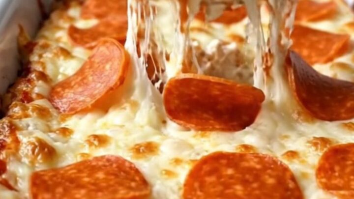 A delicious, creamy pepperoni pizza dip in a white baking dish, topped with bubbling mozzarella and pepperoni.