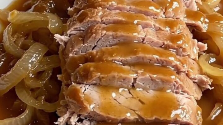 A succulent slow-cooked pork loin drizzled with a rich maple Dijon sauce on a white platter.
