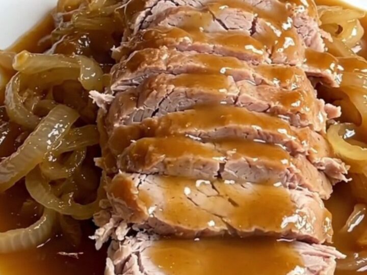 A succulent slow-cooked pork loin drizzled with a rich maple Dijon sauce on a white platter.