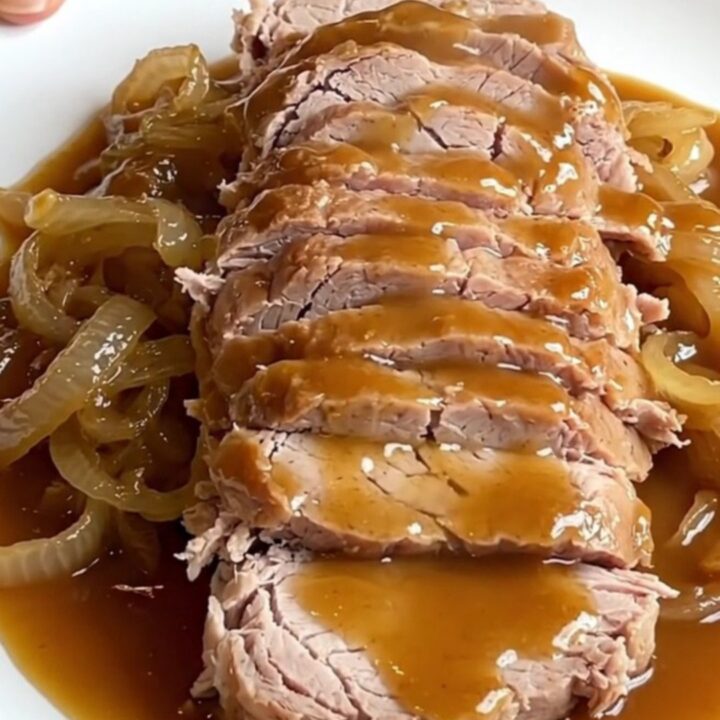 A succulent slow-cooked pork loin drizzled with a rich maple Dijon sauce on a white platter.