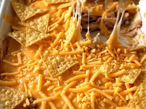 A golden, bubbly crunchwrap casserole in a white baking dish, showing layers of turkey, cheese, and chips.