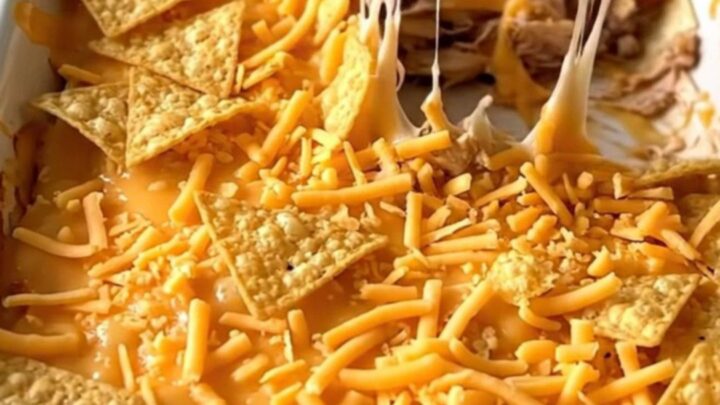 A golden, bubbly crunchwrap casserole in a white baking dish, showing layers of turkey, cheese, and chips.