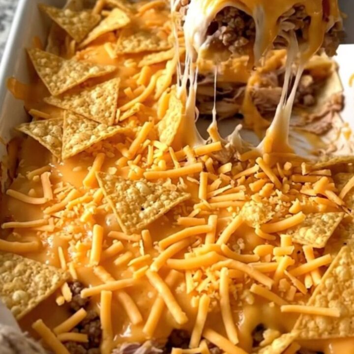 A golden, bubbly crunchwrap casserole in a white baking dish, showing layers of turkey, cheese, and chips.