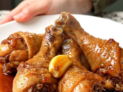 A close-up view of cooked chicken drumsticks in a dark slow cooker insert.
