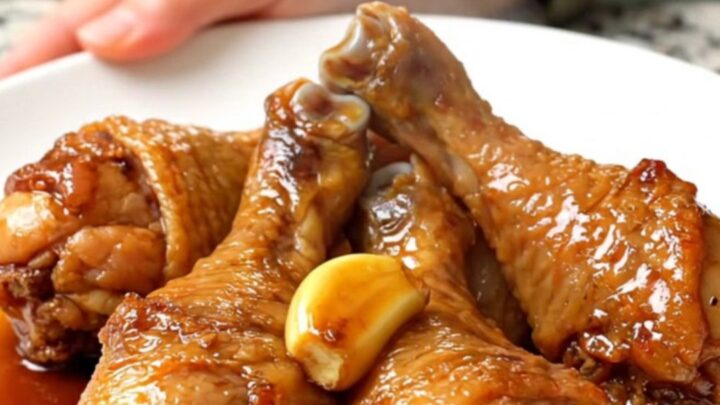 A close-up view of cooked chicken drumsticks in a dark slow cooker insert.