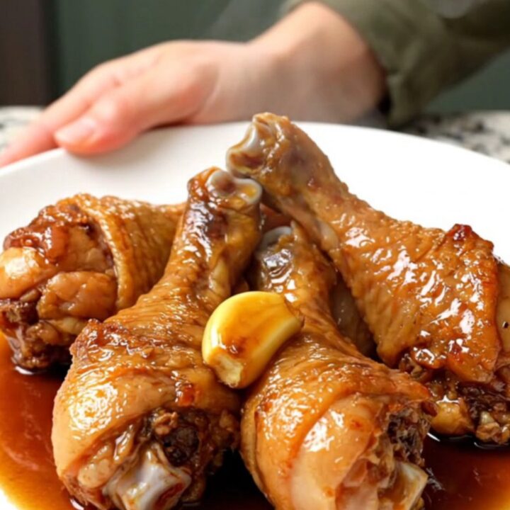 A close-up view of cooked chicken drumsticks in a dark slow cooker insert.
