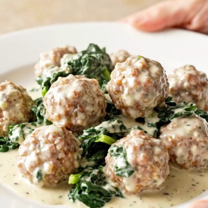 A high-angle view of a slow cooker filled with creamy turkey meatballs, wilted spinach, and rich Alfredo sauce.