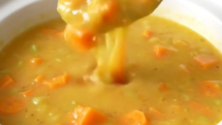 A slow cooker filled with creamy Wisconsin beer cheese soup featuring visible carrot and onion pieces.
