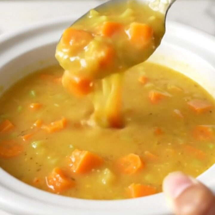 A slow cooker filled with creamy Wisconsin beer cheese soup featuring visible carrot and onion pieces.