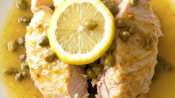 A close-up view of cooked turkey tenderloins in a slow cooker, surrounded by lemon slices and capers in a buttery sauce.