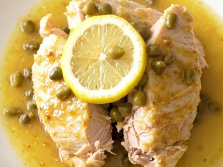 A close-up view of cooked turkey tenderloins in a slow cooker, surrounded by lemon slices and capers in a buttery sauce.