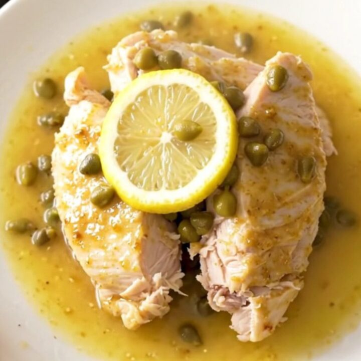 A close-up view of cooked turkey tenderloins in a slow cooker, surrounded by lemon slices and capers in a buttery sauce.