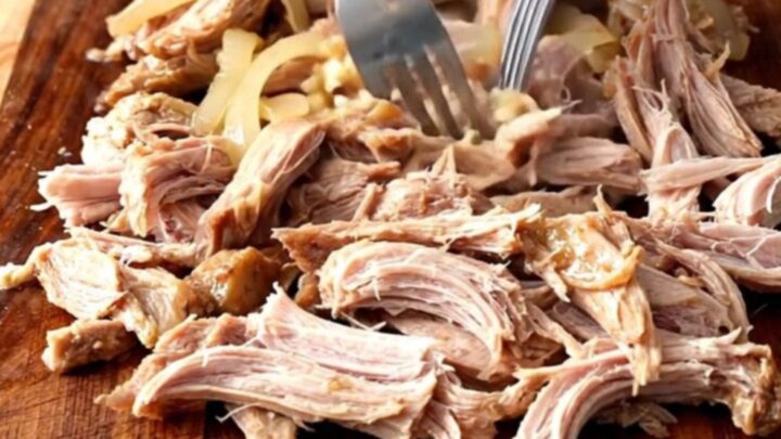 A close-up of tender, shredded mojo pork inside a slow cooker, showcasing the vibrant citrus juices and soft onions.