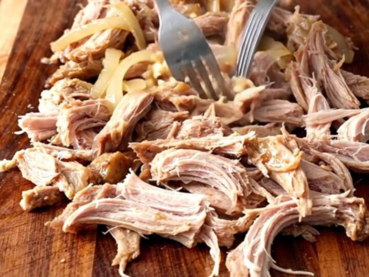 A close-up of tender, shredded mojo pork inside a slow cooker, showcasing the vibrant citrus juices and soft onions.