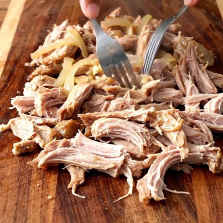 A close-up of tender, shredded mojo pork inside a slow cooker, showcasing the vibrant citrus juices and soft onions.