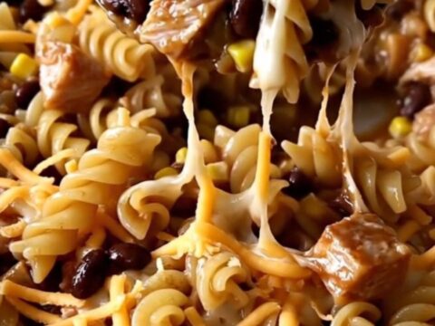 A top-down view of a rectangular baking dish filled with raw rotini, ground turkey, barbecue sauce, and shredded cheese.