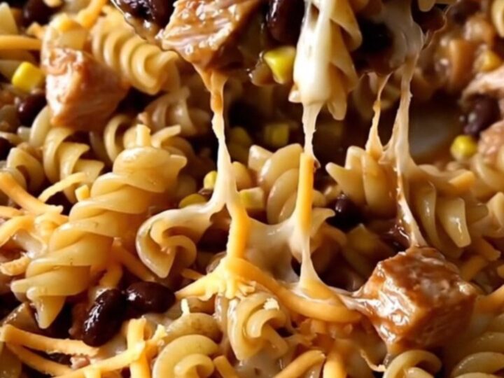 A top-down view of a rectangular baking dish filled with raw rotini, ground turkey, barbecue sauce, and shredded cheese.
