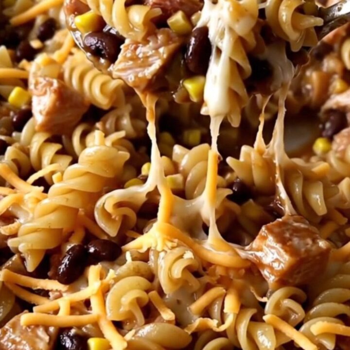 A top-down view of a rectangular baking dish filled with raw rotini, ground turkey, barbecue sauce, and shredded cheese.