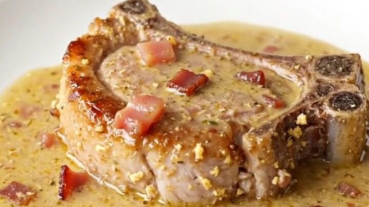 A close-up of a juicy, braised pork chop covered in a thick, creamy bacon-flecked gravy in a slow cooker.