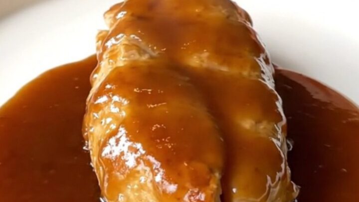 A close-up of tender braised honey barbecue chicken breasts with soft onions in a slow cooker.