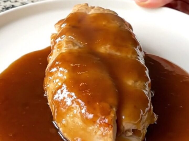 A close-up of tender braised honey barbecue chicken breasts with soft onions in a slow cooker.