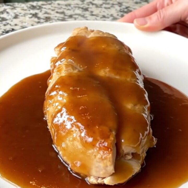 A close-up of tender braised honey barbecue chicken breasts with soft onions in a slow cooker.