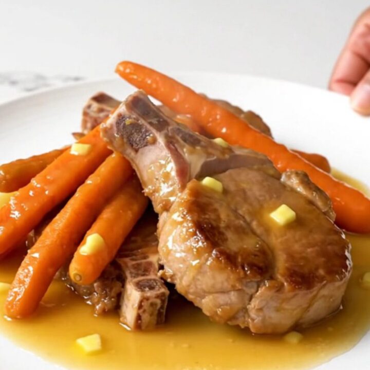 Close-up of tender slow-cooked pork chops and baby carrots glazed in a glossy honey butter sauce.