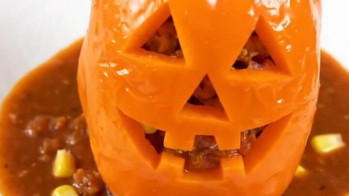 Four orange bell peppers carved with jack-o'-lantern faces, stuffed with a savory turkey and corn filling.
