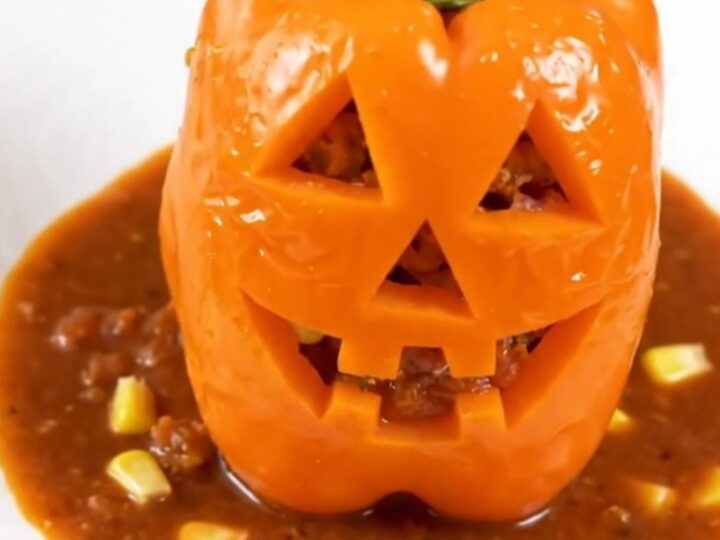 Four orange bell peppers carved with jack-o'-lantern faces, stuffed with a savory turkey and corn filling.