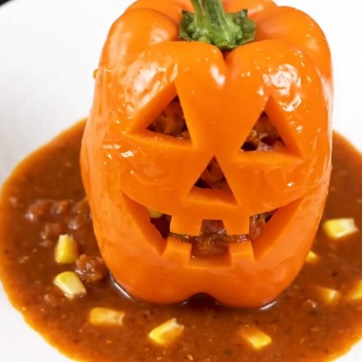 Four orange bell peppers carved with jack-o'-lantern faces, stuffed with a savory turkey and corn filling.