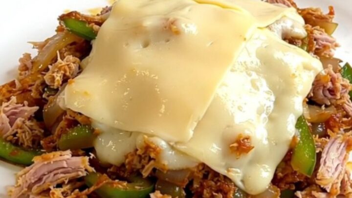 A close-up view of the slow cooker filled with cooked turkey, peppers, onions, and melted provolone cheese.