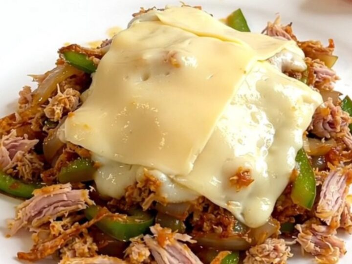 A close-up view of the slow cooker filled with cooked turkey, peppers, onions, and melted provolone cheese.