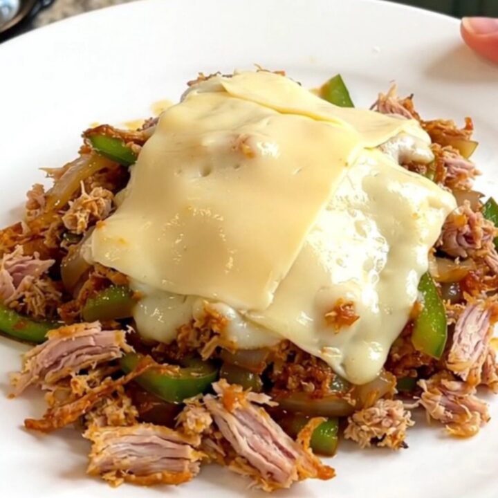 A close-up view of the slow cooker filled with cooked turkey, peppers, onions, and melted provolone cheese.