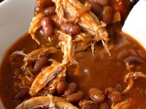 A top-down view of a steaming bowl of smoky honey chicken chili with shredded chicken and pinto beans.