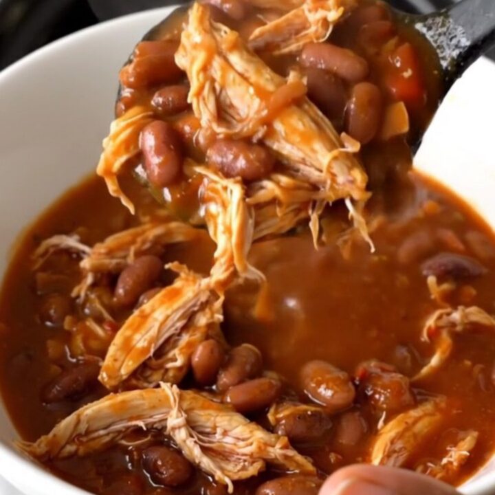 A top-down view of a steaming bowl of smoky honey chicken chili with shredded chicken and pinto beans.