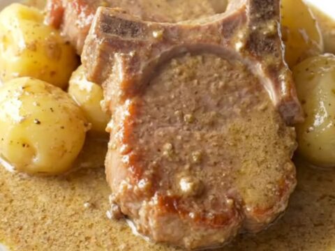 A close-up of tender, slow-cooked pork chops covered in a rich, creamy mushroom gravy with soft baby potatoes.